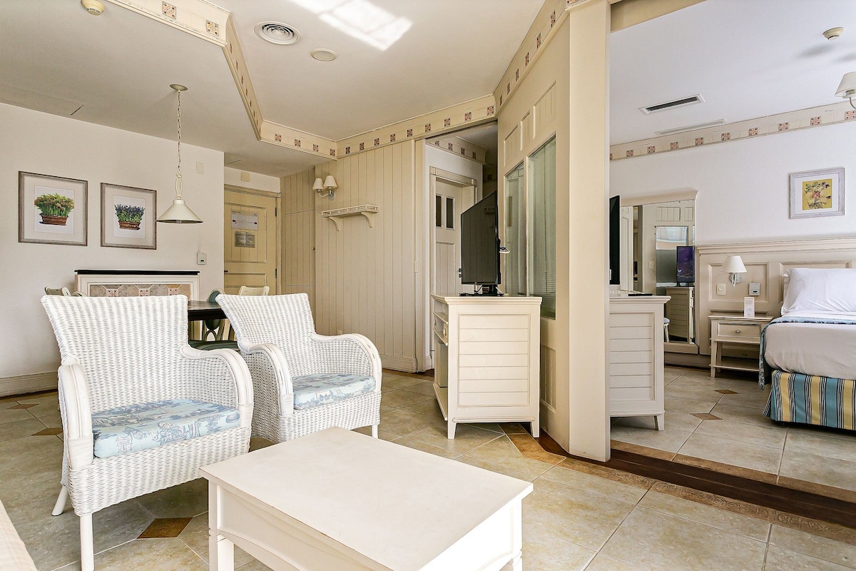 Habitación de hotel con cama, escritorio, dos sillas de mimbre, una mesita, cómoda y espejo.