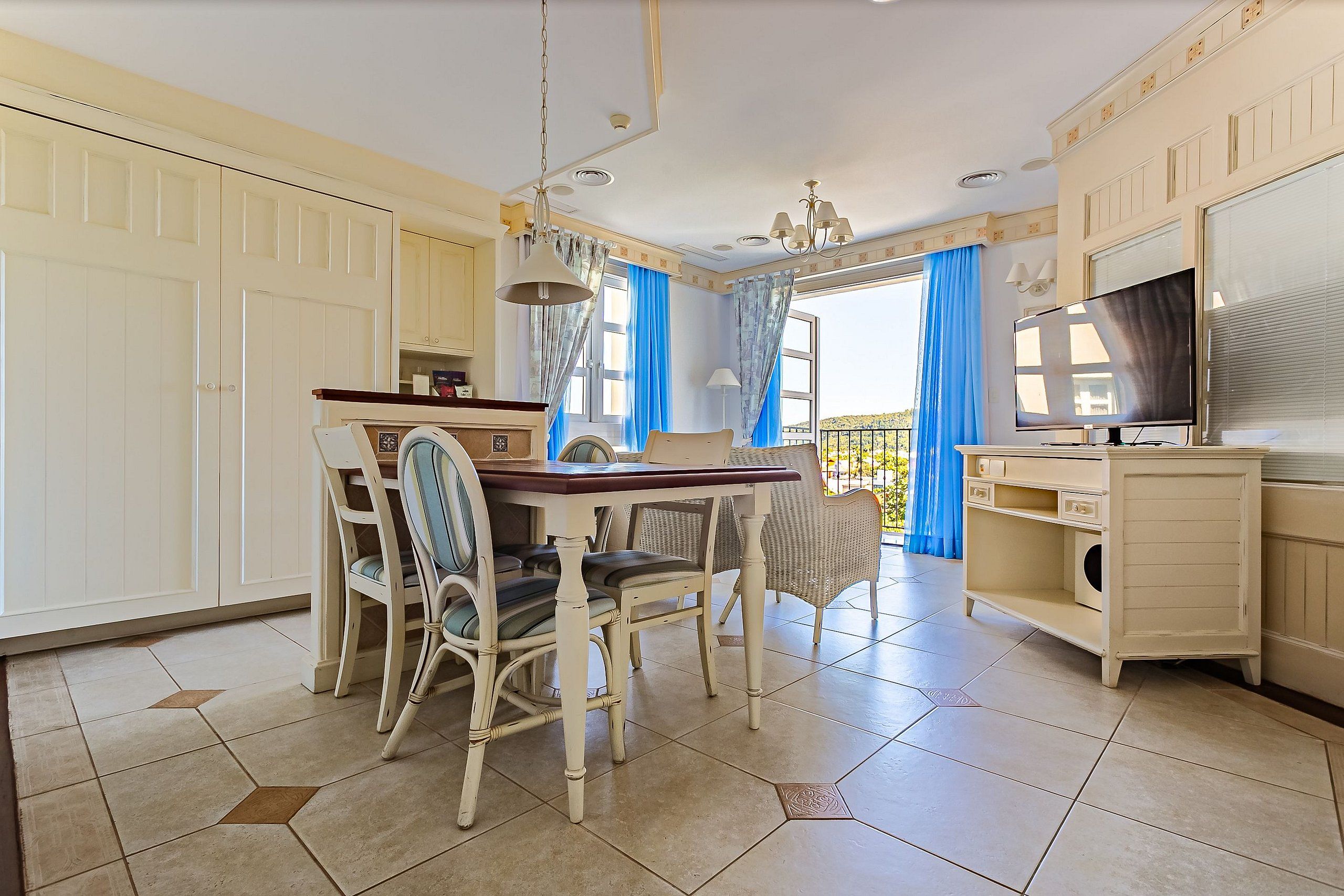 A dining area with a table and chairs, a television, and a balcony with curtains.