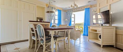 A dining area with a table and chairs, a television, and a balcony with curtains.