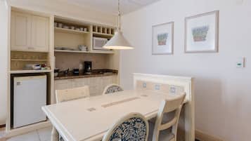 A kitchen with white cabinets, a white refrigerator, a microwave, and a dining table with chairs. There are two framed pictures on the wall.