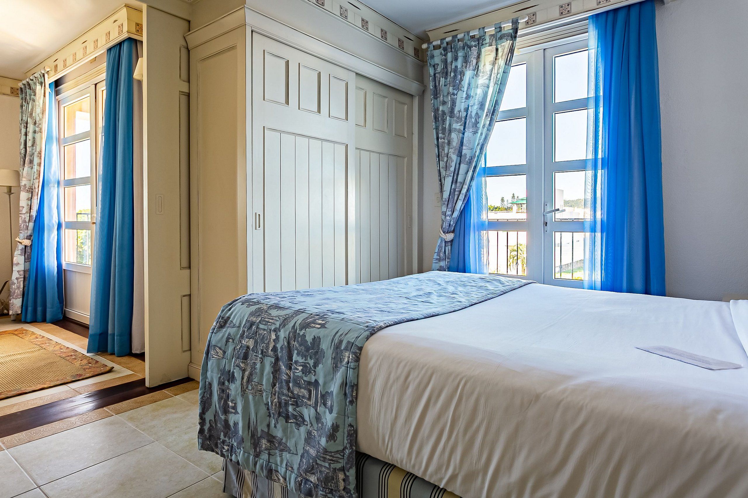 Un dormitorio con cama, armario y ventana con cortinas azules.