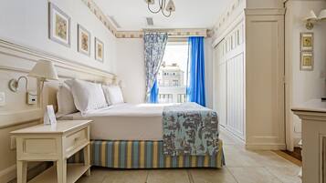 A hotel room with a bed, a nightstand, a lamp, a window with blue curtains, and a view of buildings outside.