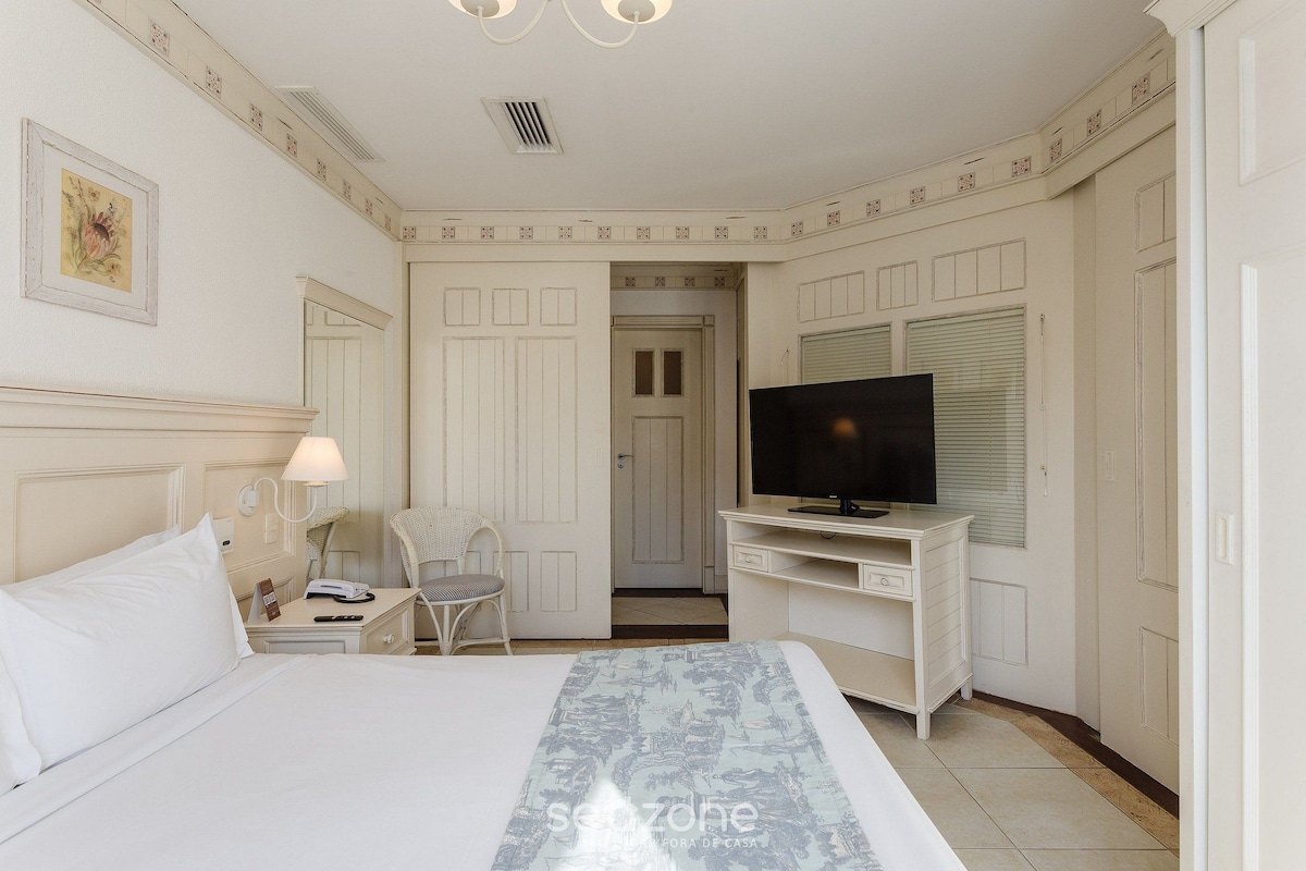 Una habitación de hotel con una cama, un escritorio con televisor, una silla y una lámpara.