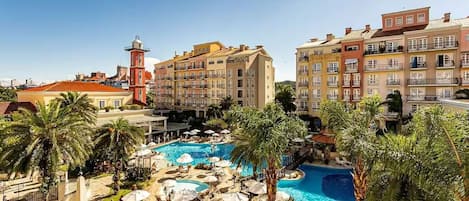 Un resort con piscina central, palmeras y edificios de varios pisos con balcones.