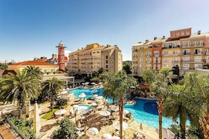 Un resort con piscina central, palmeras y edificios de varios pisos con balcones.