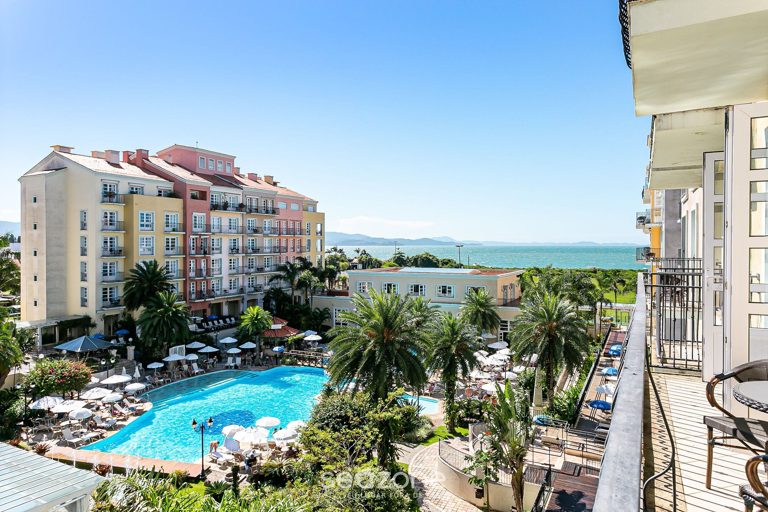 A hotel with a swimming pool surrounded by palm trees and lounge chairs.