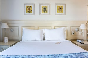 Habitación de hotel con una cama grande, dos mesitas de noche y tres cuadros enmarcados con motivos florales en la pared.
