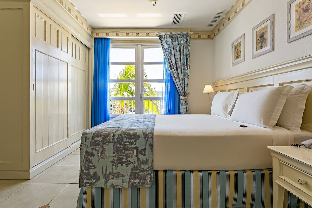 Una habitación de hotel con cama, mesita de noche, lámpara y ventana con cortinas azules.