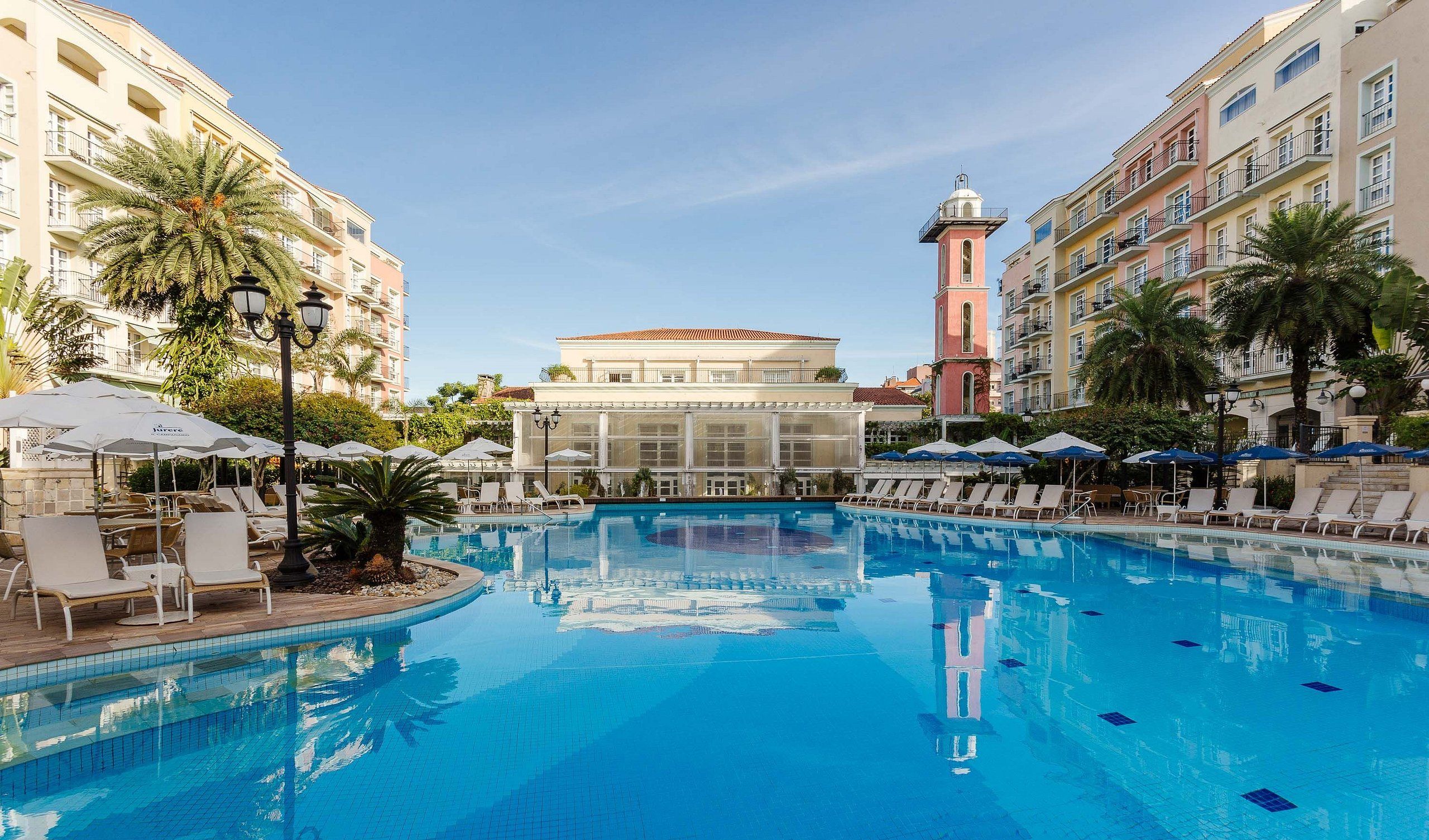 A swimming pool with lounge chairs and umbrellas, surrounded by multi-story buildings with balconies.