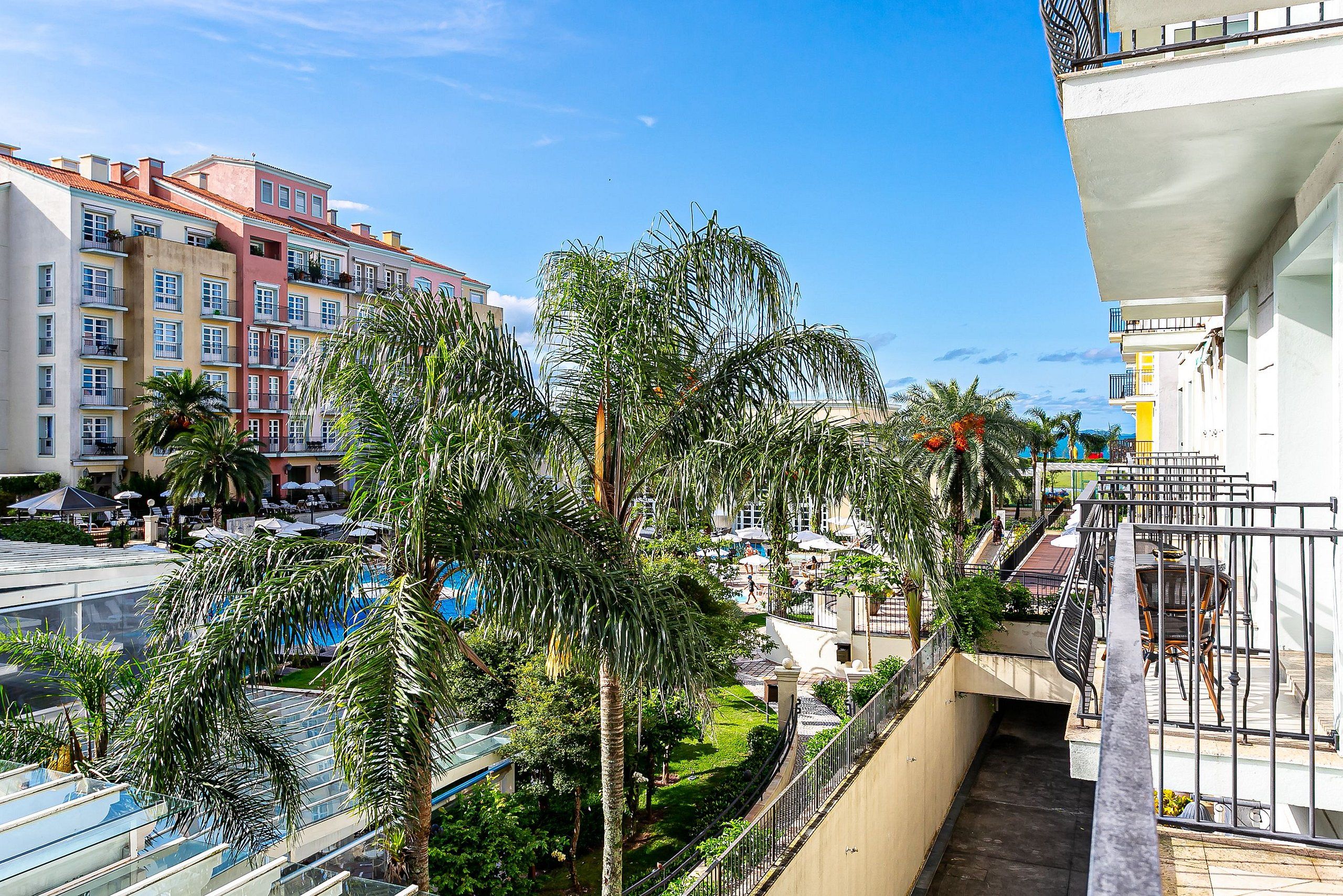 A multi-story hotel with balconies, palm trees, and a clear blue sky.