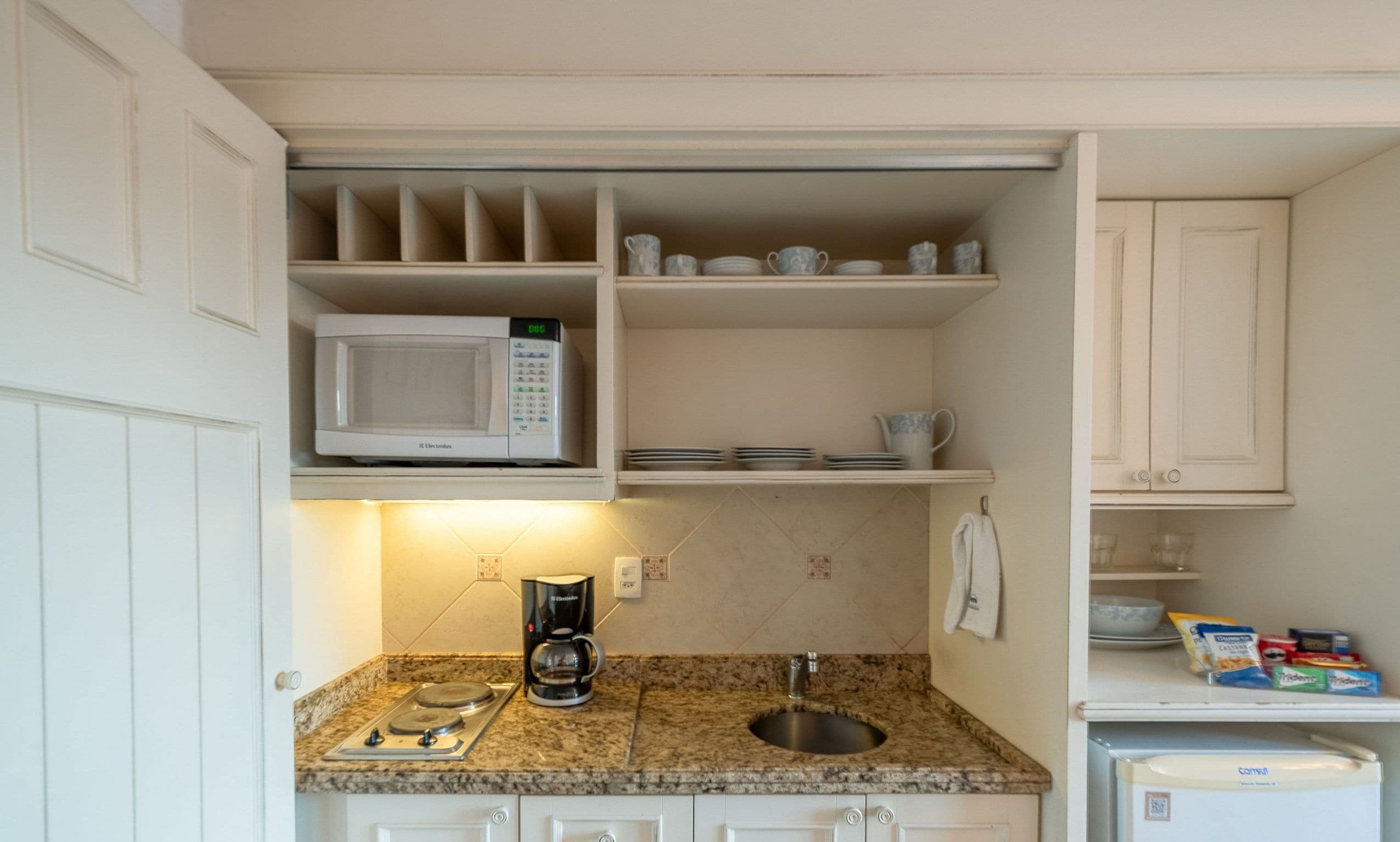 Una cocina compacta con microondas, cafetera y un refrigerador pequeño.
