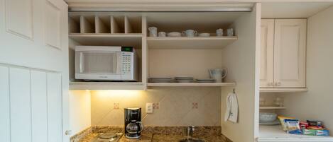 Una cocina compacta con microondas, cafetera y un refrigerador pequeño.