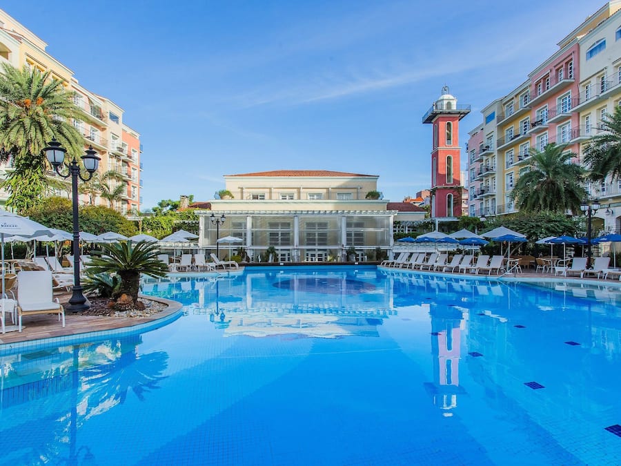 A swimming pool with lounge chairs and umbrellas, surrounded by multi-story buildings with balconies.