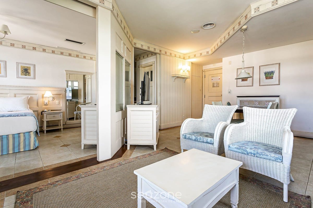 Habitación de hotel con cama, un pequeño escritorio, dos sillas de mimbre, una mesa blanca y un espejo.
