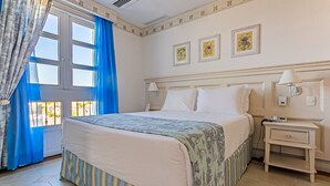 A hotel room with a large bed, a bedside table, a nightstand, and a window with blue curtains. - Studios frente ao mar no IL Campanario Resort ILCTOP (Florianópolis)