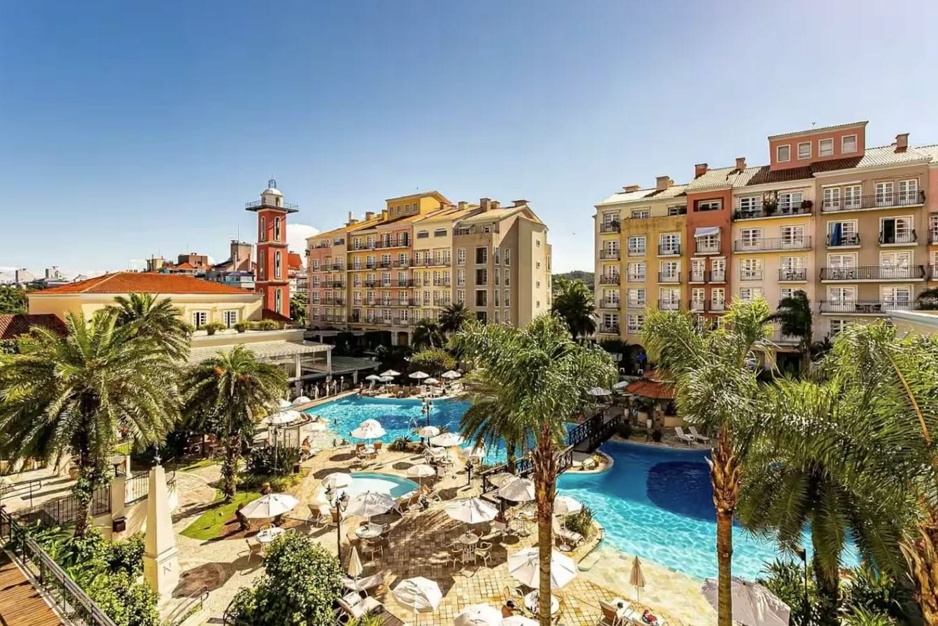 Un hotel con piscina rodeada de palmeras y zonas de estar al aire libre.