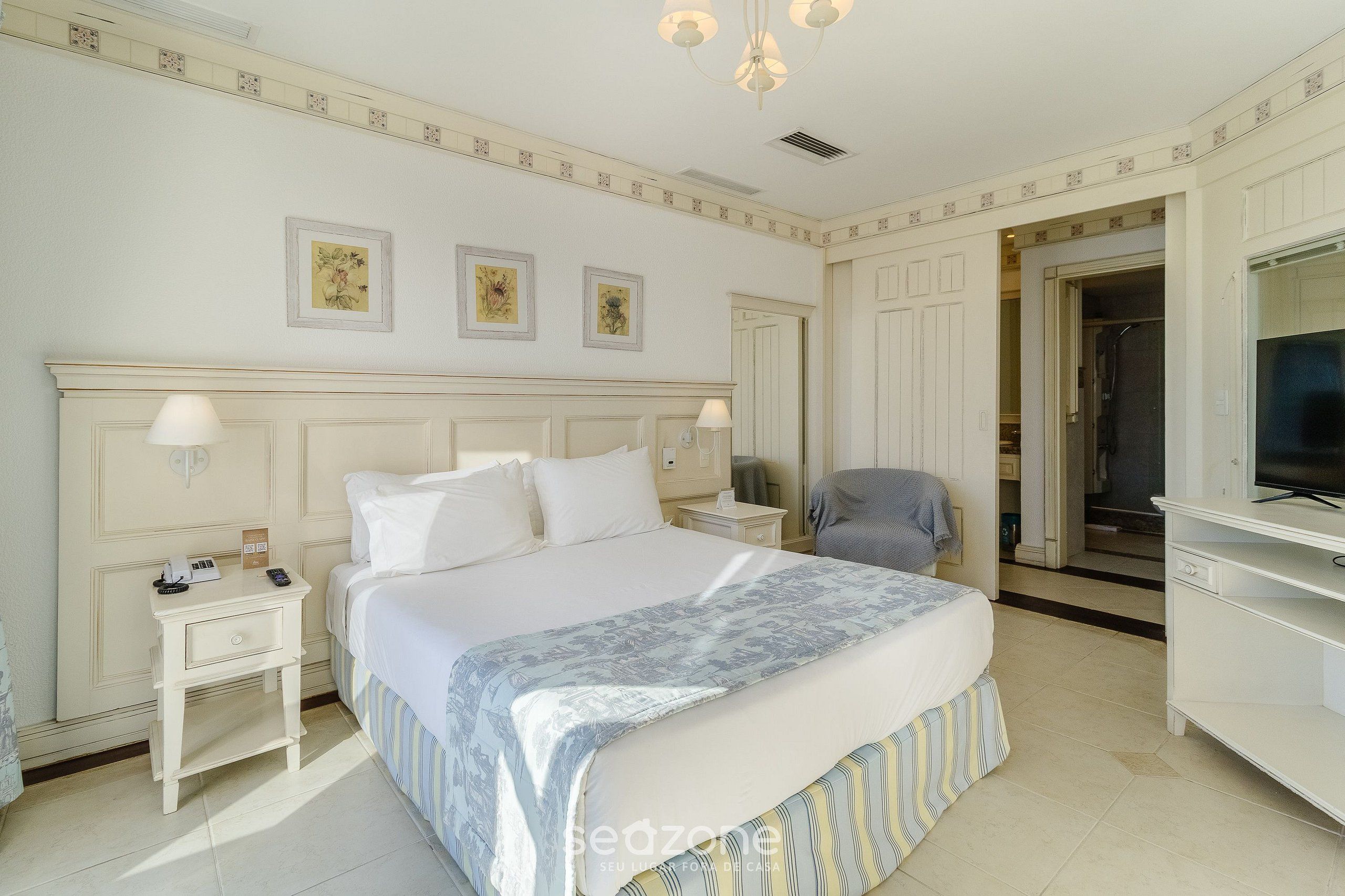 A hotel room with a large bed, bedside tables, a chair, a TV, and a wardrobe.