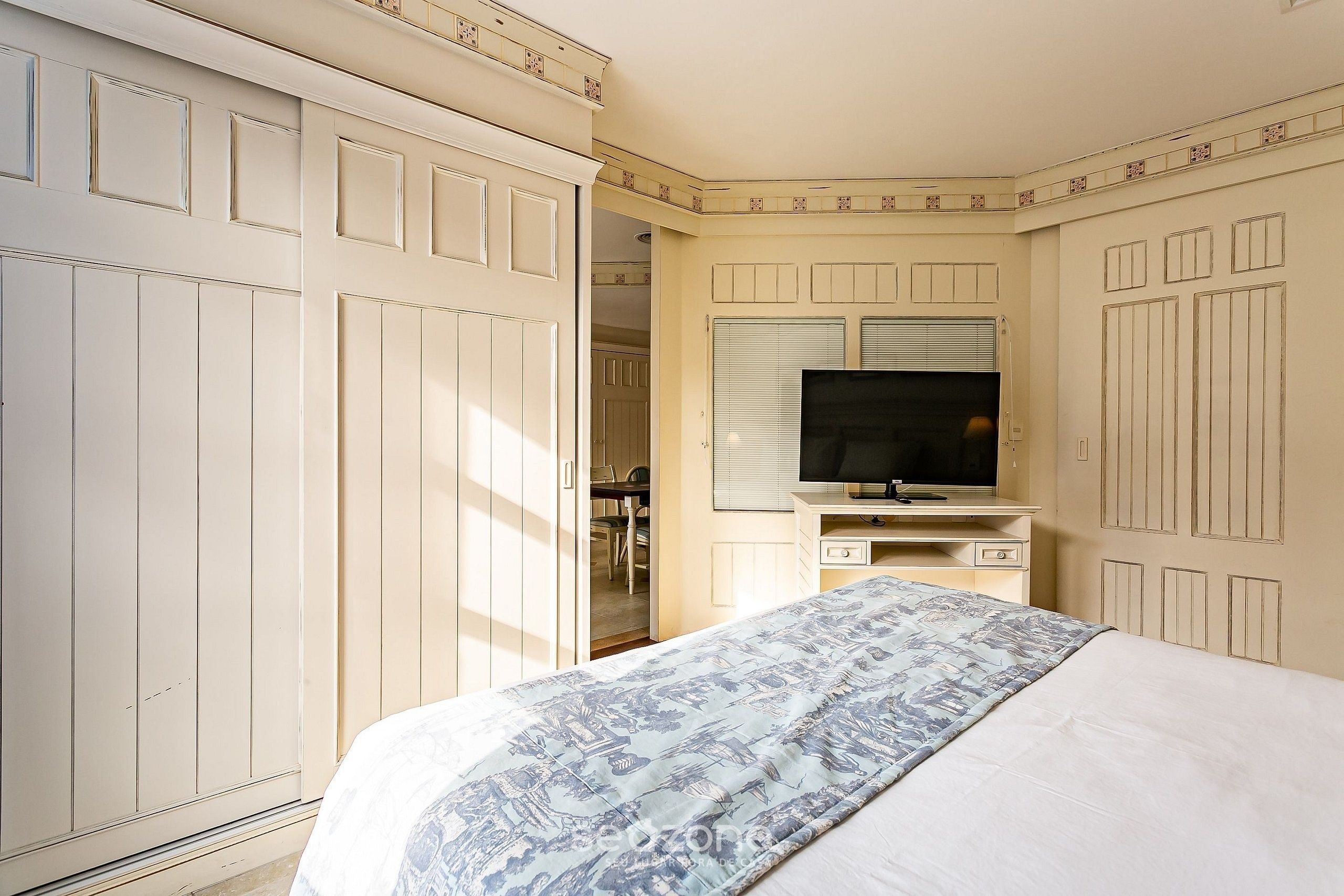Un dormitorio con cama, televisor sobre un mueble bajo y armario.