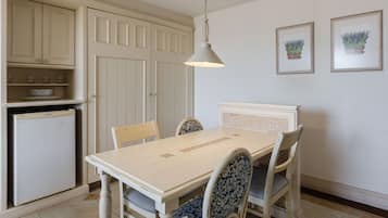 Un comedor con mesa y sillas blancas, una lámpara colgante y un refrigerador.
