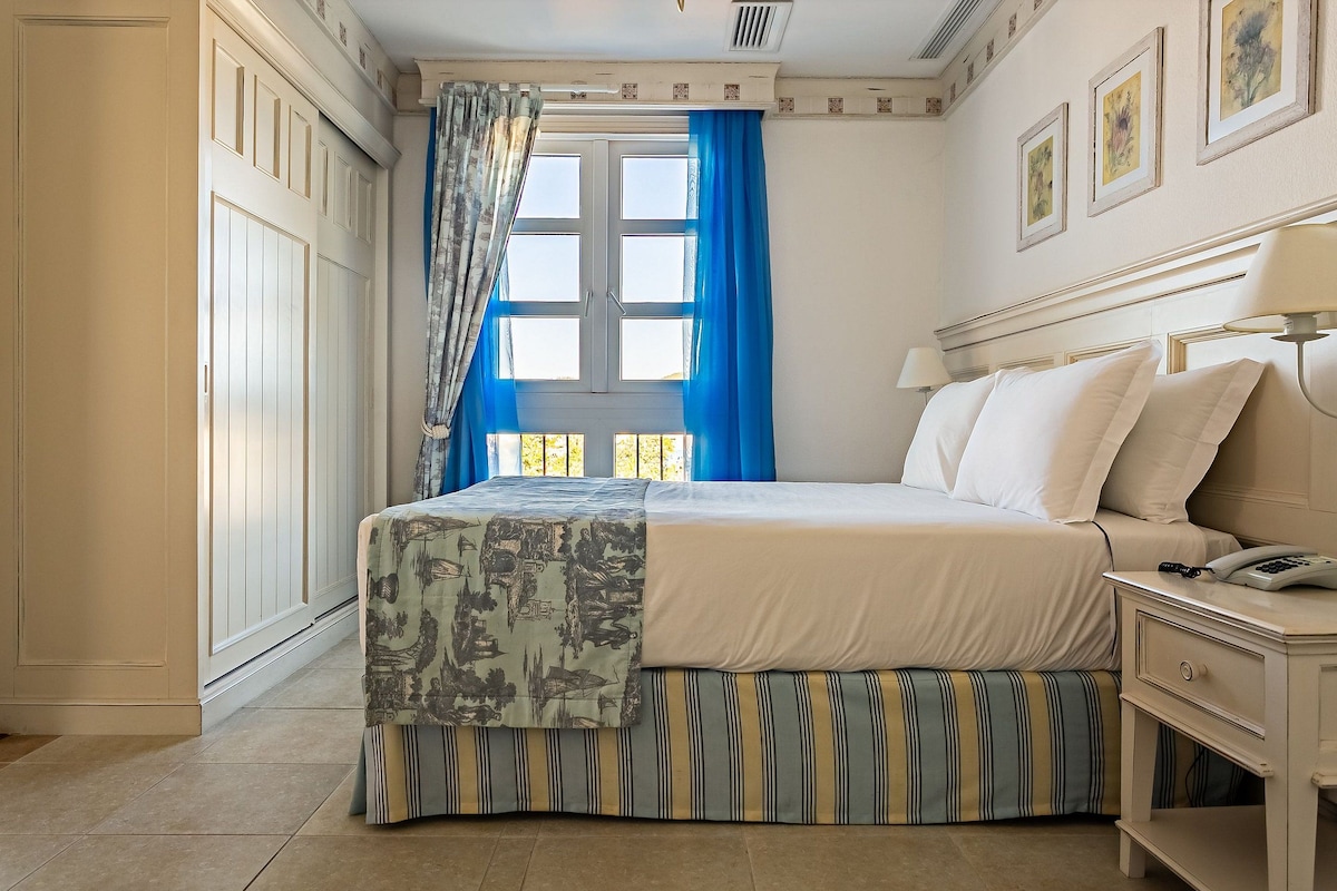 Un dormitorio ordenado con cama, mesita de noche y ventana con cortinas.