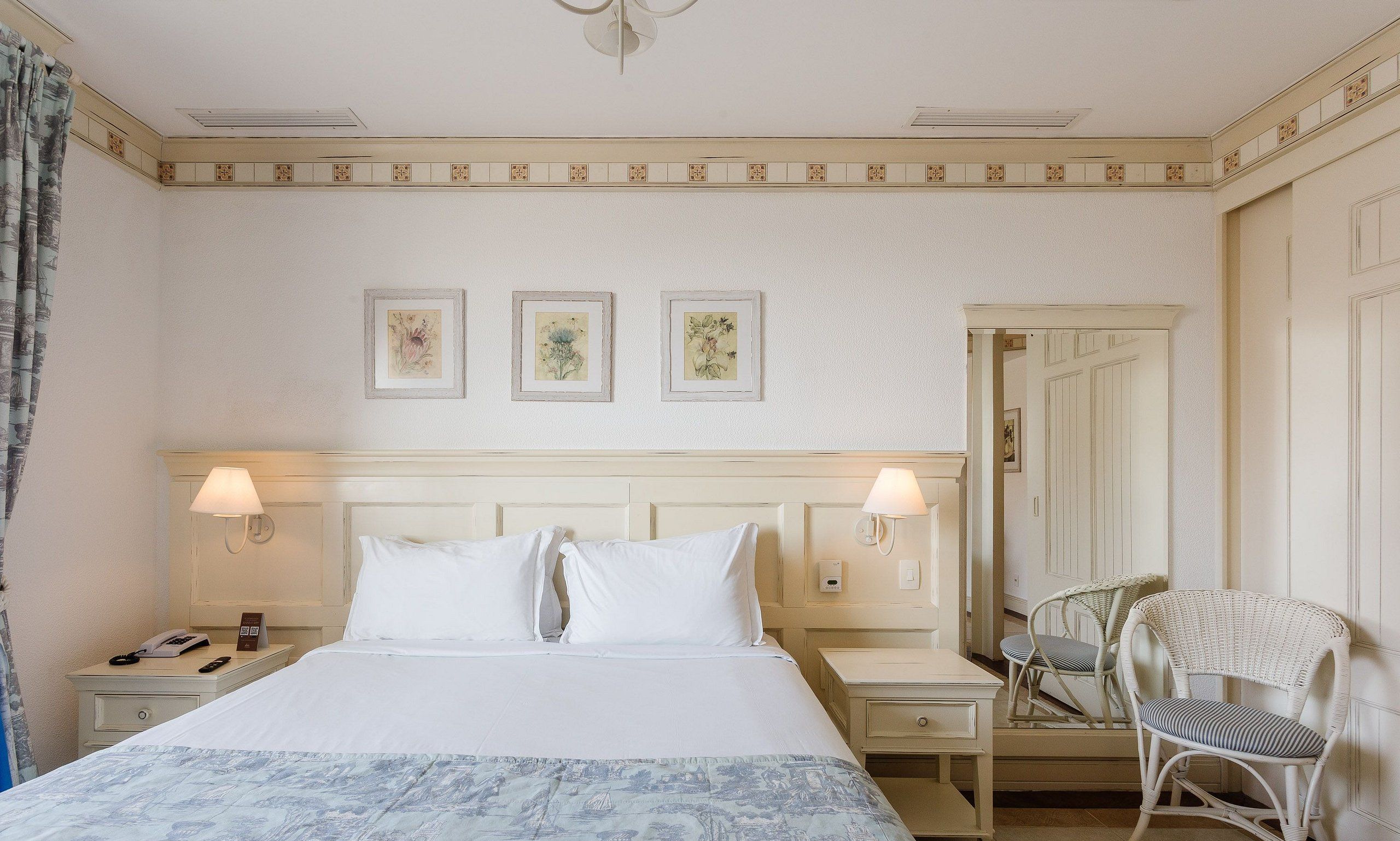 Una habitación de hotel con una cama, dos lámparas de noche, una mesita de noche, una silla y una puerta.