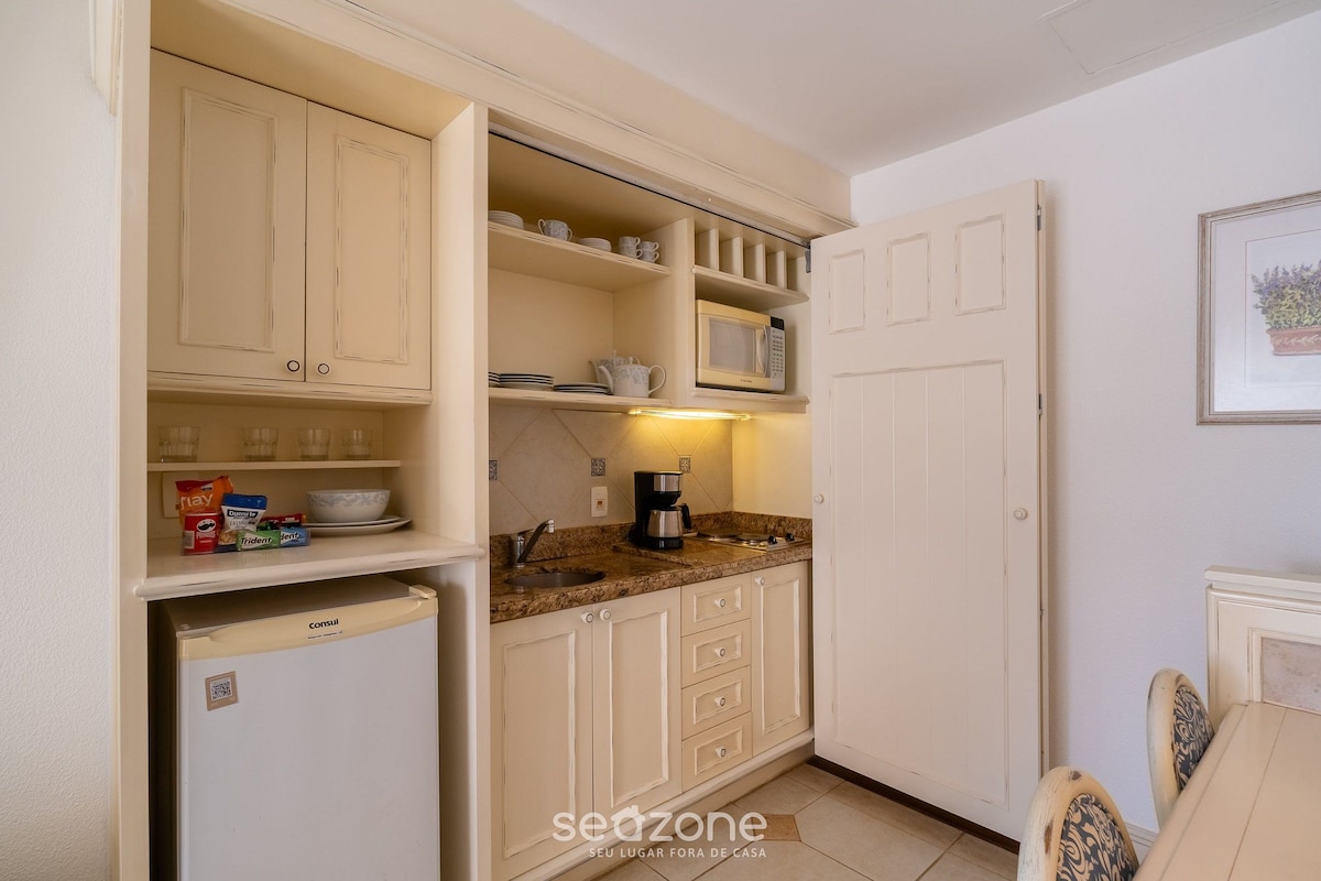 Una cocina compacta con armarios blancos, un microondas integrado y una cafetera.