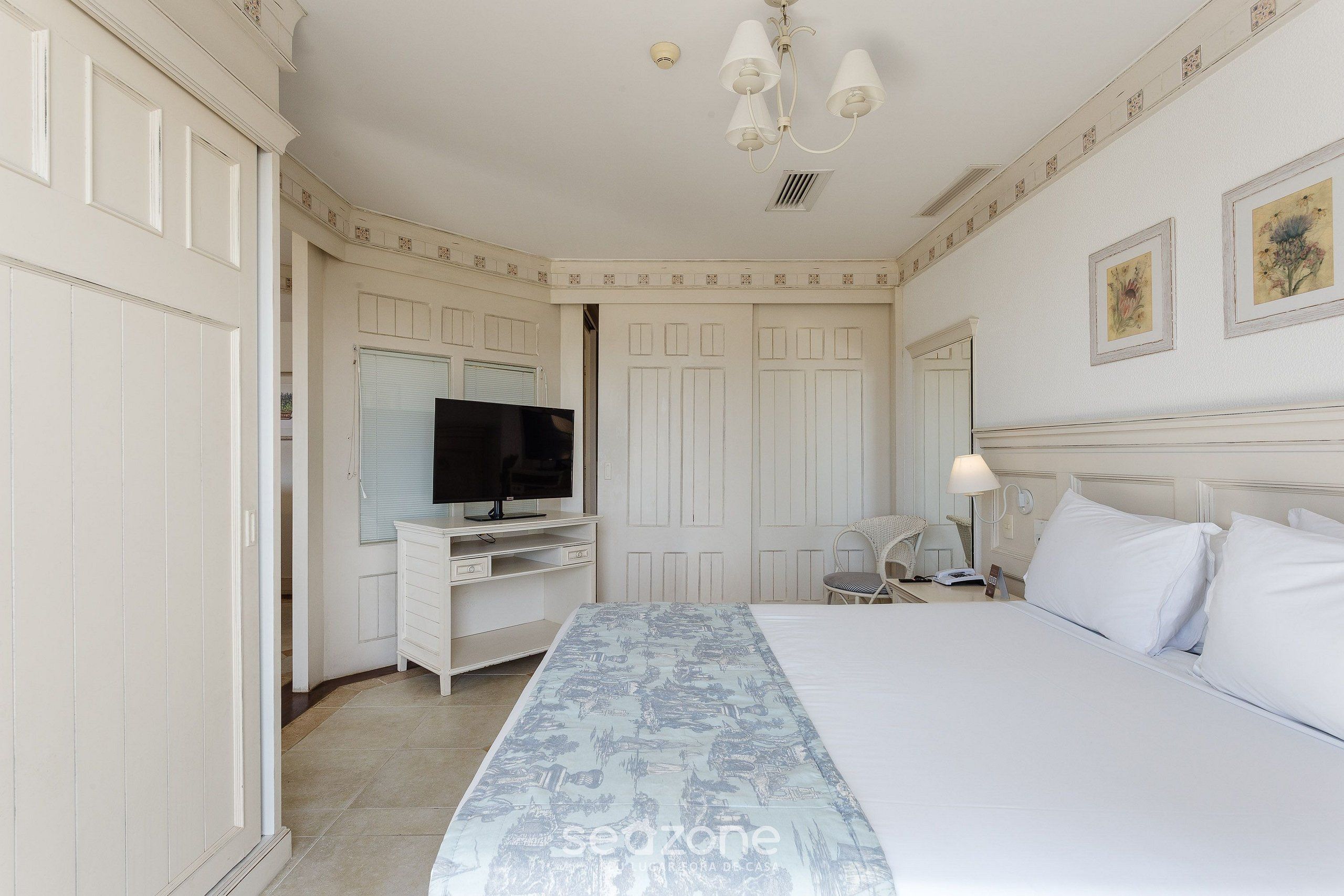 Habitación de hotel con una cama grande, un televisor en un mueble bajo, un escritorio con silla y una mesita de noche con lámpara.