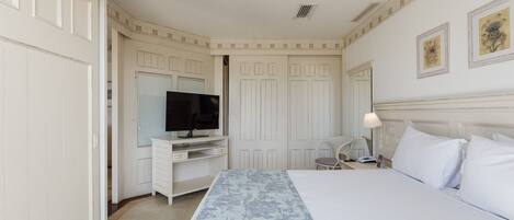 Habitación de hotel con una cama grande, un televisor en un mueble bajo, un escritorio con silla y una mesita de noche con lámpara.
