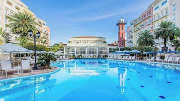 A swimming pool with lounge chairs and umbrellas, surrounded by multi-story buildings with balconies.