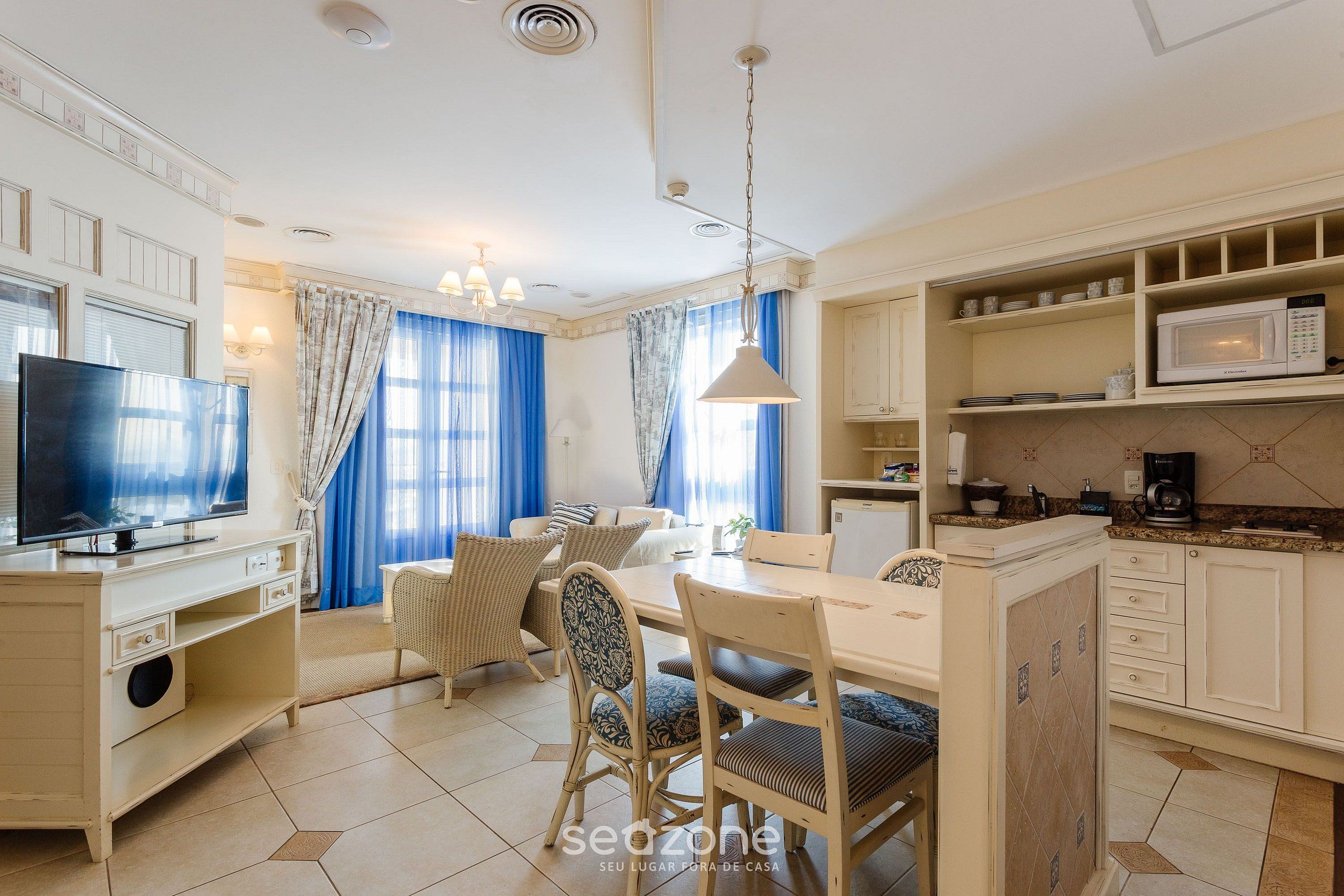 Una habitación luminosa con una mesa de comedor, sillas, televisor y una zona de cocina con microondas.