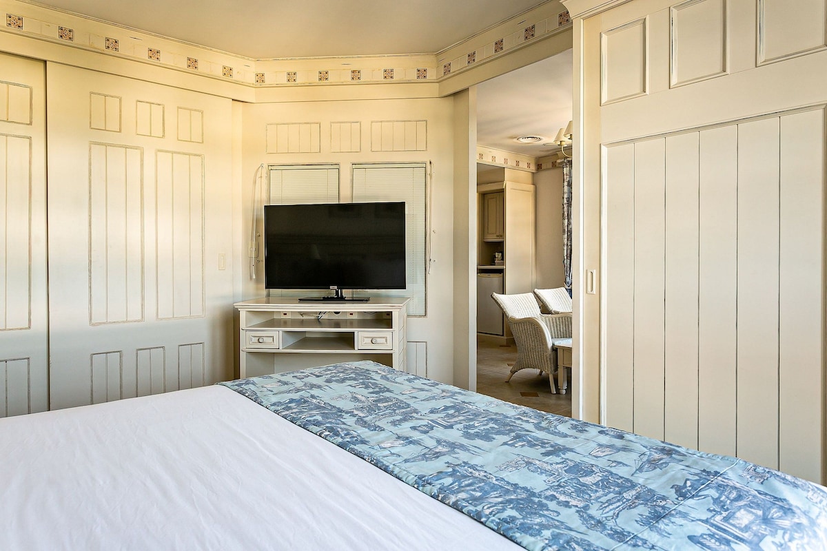Un dormitorio con una cama, un televisor sobre un mueble bajo y un escritorio con una silla.