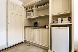 Una cocina con gabinetes blancos, microondas, cafetera y refrigerador.