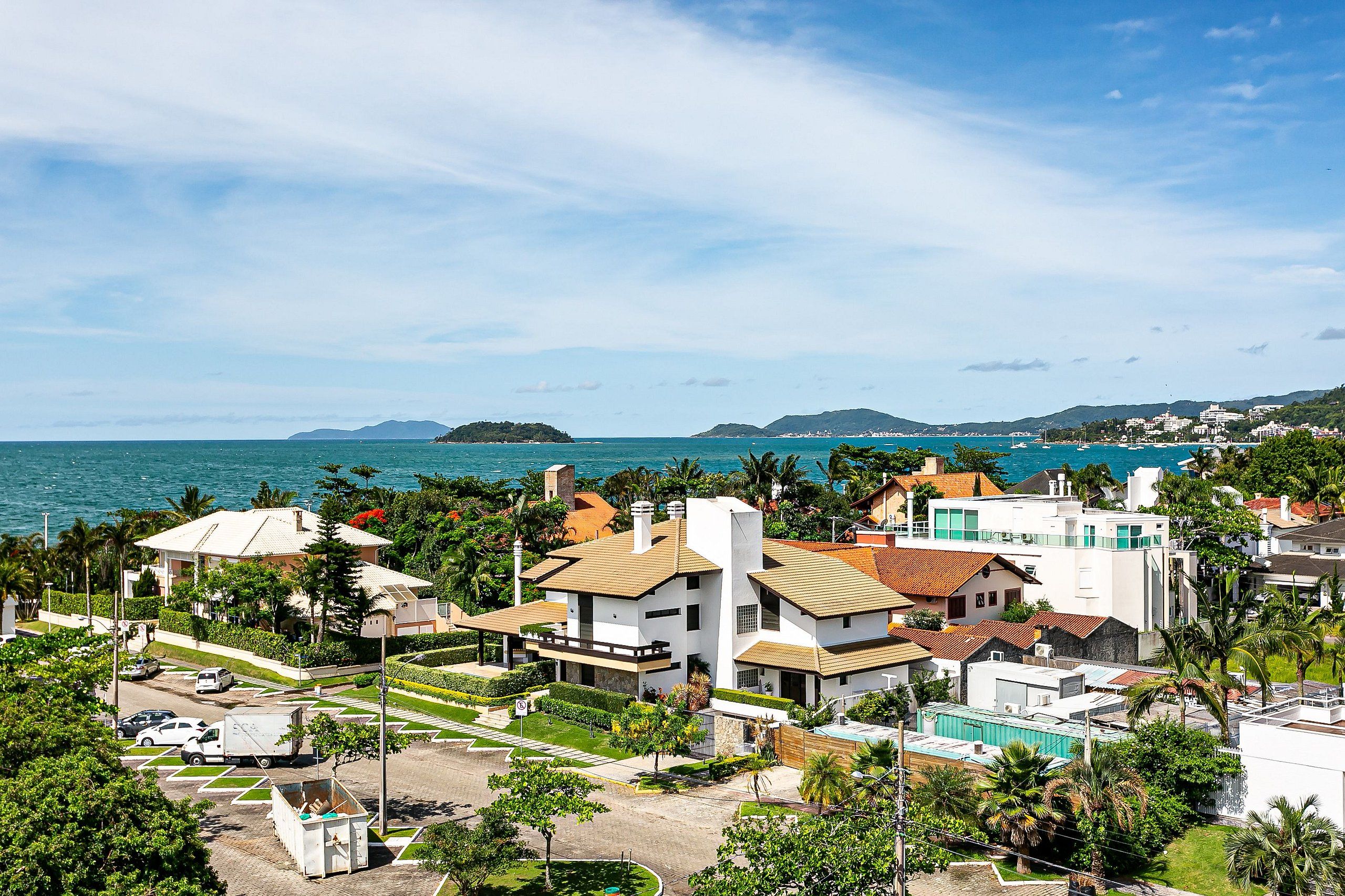 A coastal residential area with modern houses, a parking lot, and a view of the sea and distant islands.