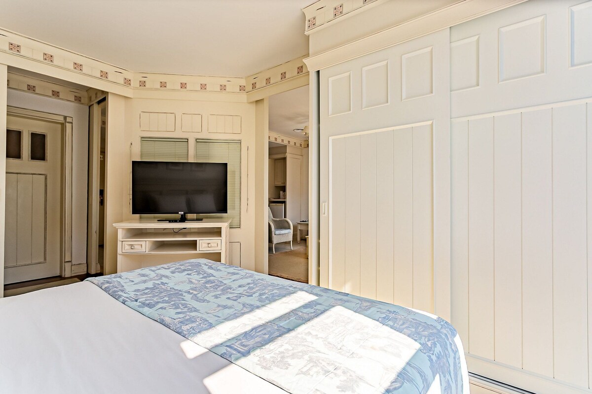 Un dormitorio con una cama, un televisor sobre un mueble, un armario y una puerta que da a otra habitación.