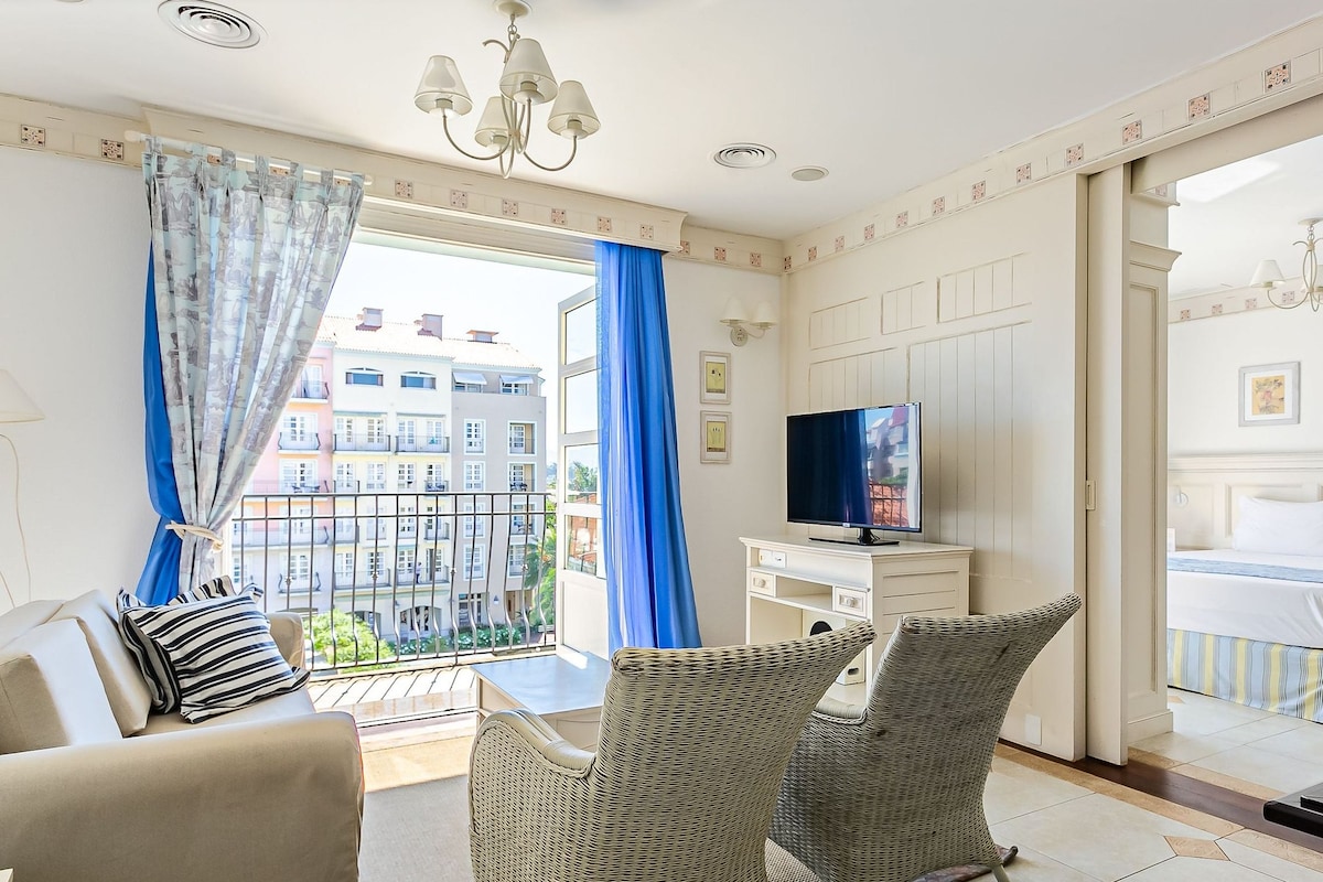 Una habitación de hotel con balcón, televisión, cama y sillones de mimbre.