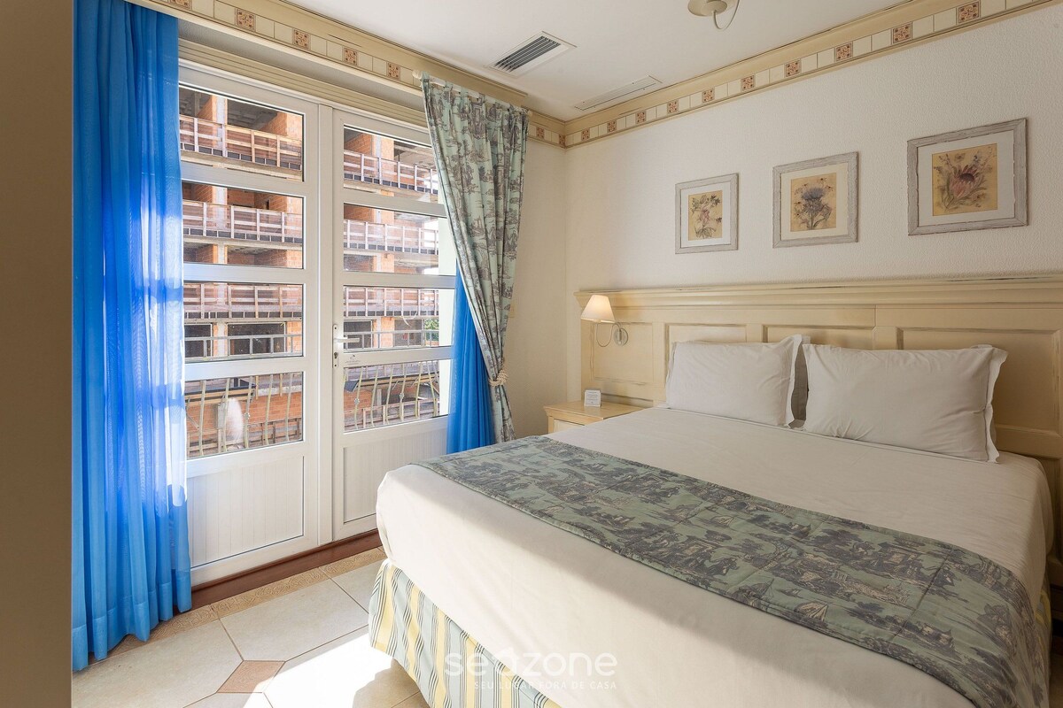 Una habitación de hotel con una cama grande, una ventana con cortinas azules y tres cuadros en la pared.