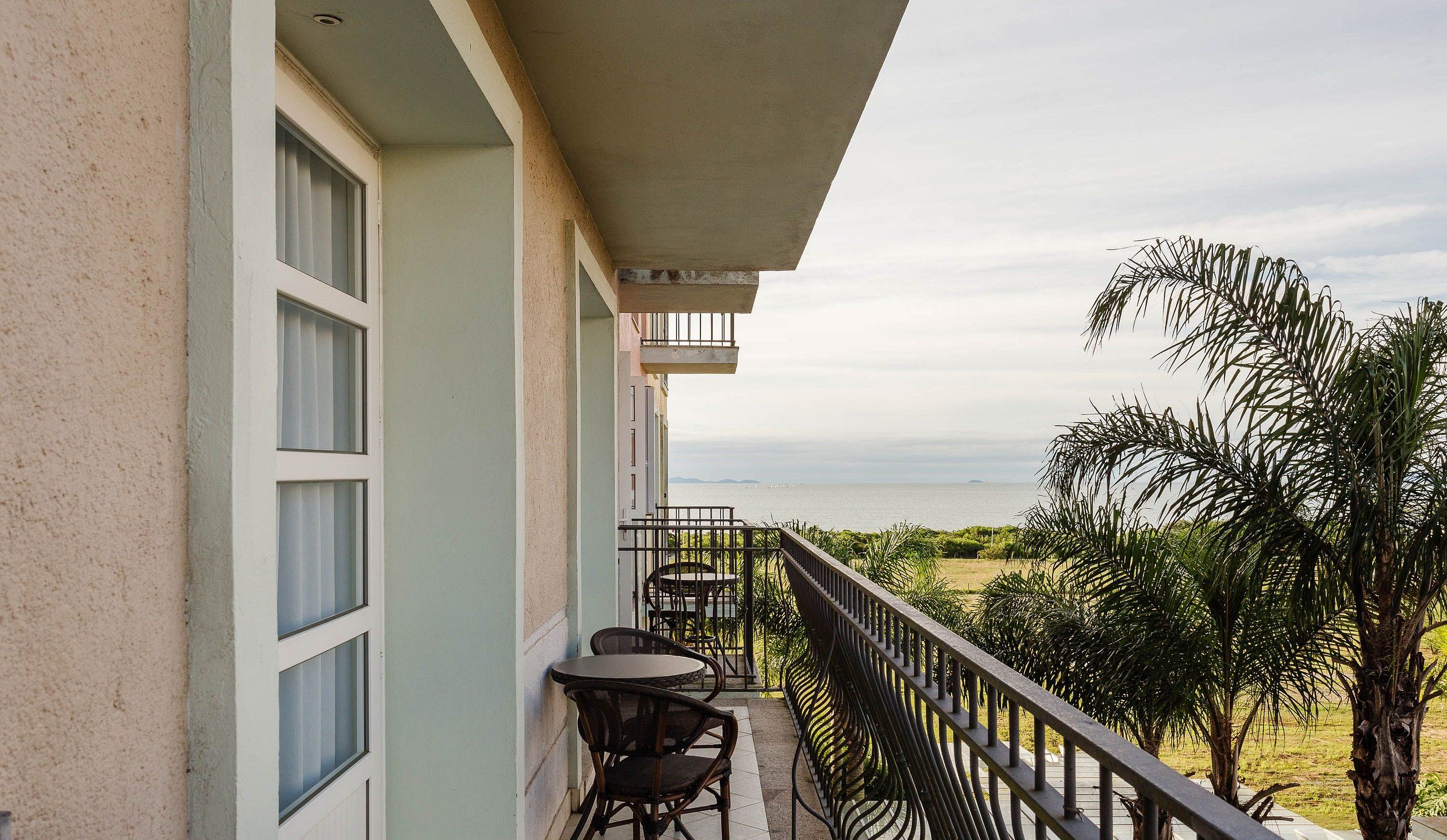 A balcony with a table and chairs, overlooking a body of water and greenery.