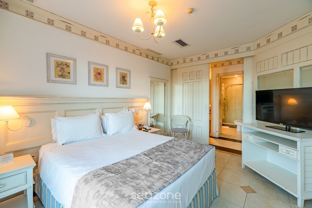 A hotel room with a large bed, a TV, a desk, and a chair.