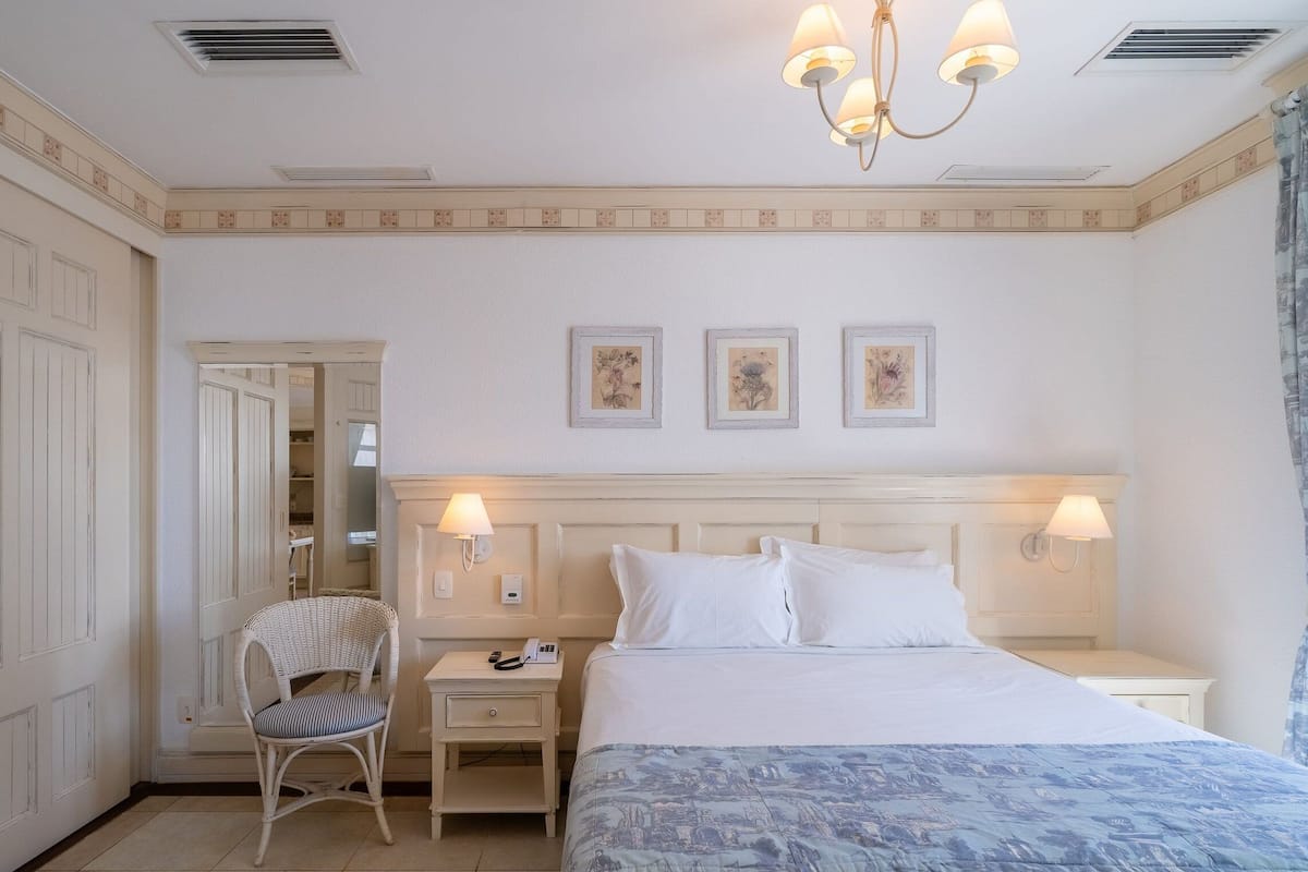 Una habitación de hotel con una cama, una mesita de noche, una silla, un armario y una araña.