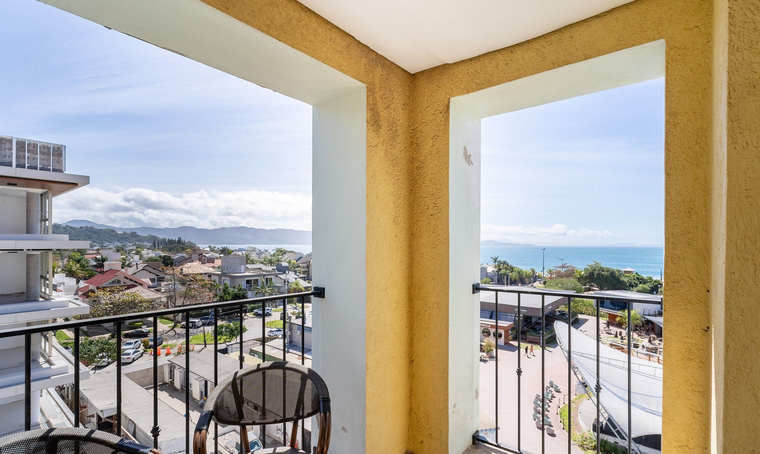 A balcony with a view of a coastal town, a chair, and a building with a sign that reads "DURAN".