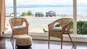 A room with two wicker chairs facing a large window overlooking a parking area and a body of water. - Beachfront | Sandy Shore, Near Mt. Washington (Campbell River)