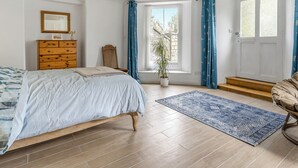 Een slaapkamer met een bed, een dressoir, een stoel, een raam en een potplant.