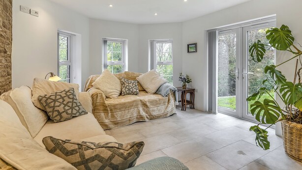 Een ruime woonkamer met een beige bank, een gebreid plaid en een grote plant.