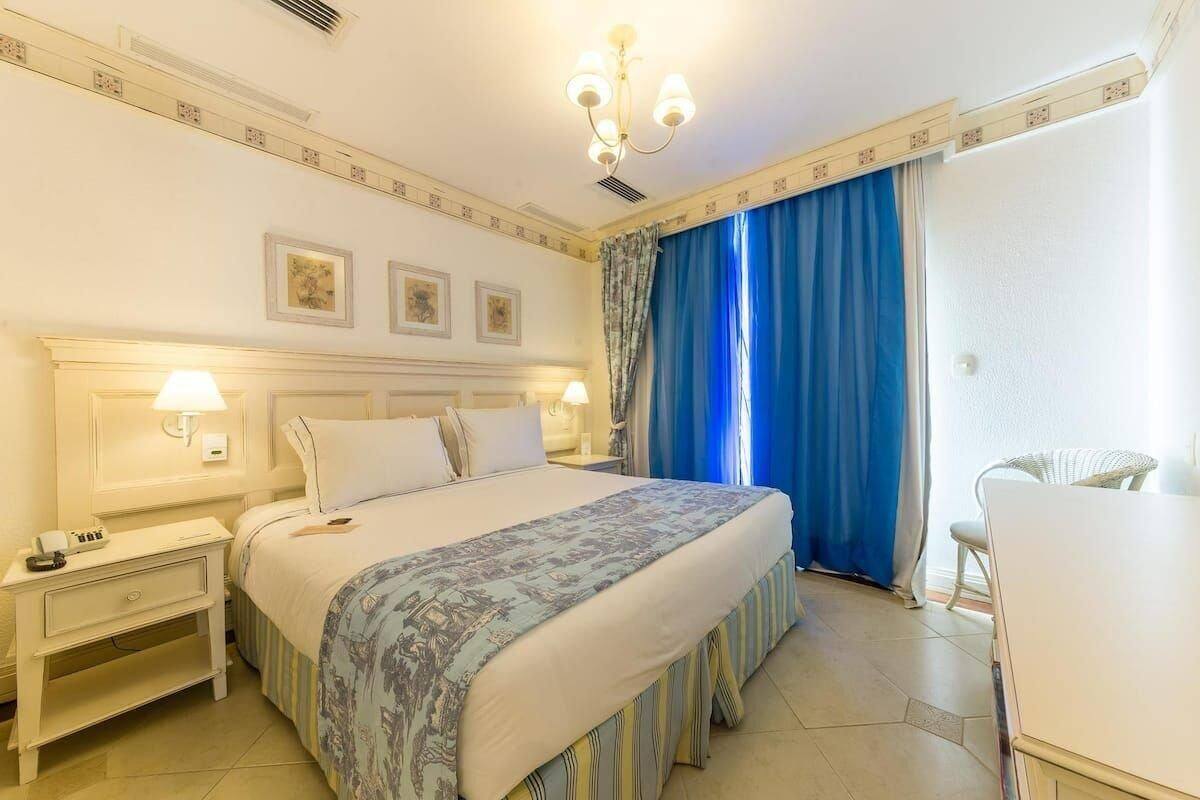 Ein Hotelzimmer mit einem Bett, Nachttischen, einem Sessel und einem Fenster mit Vorhängen.