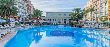A swimming pool with lounge chairs and umbrellas, surrounded by multi-story buildings with balconies.