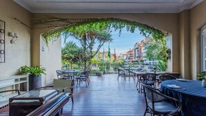 Un patio al aire libre con mesas y sillas, rodeado de follaje y vistas a edificios.