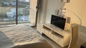 Ett modernt sovrum med en stor säng, en tv på ett vitt skåp och utsikt över staden genom fönstret.