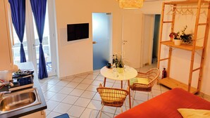 A compact living space with a dining area, a TV mounted on the wall, a wooden shelf with a plant, and a red sofa. - Raito Guest House - Amalfi Coast (Vietri sul Mare)
