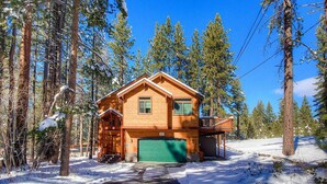 A wooden cabin with a green garage door, surrounded by tall pine trees and snow on the ground. - Enormous luxury cabin rental in unbeatable South Tahoe location (South Lake Tahoe)