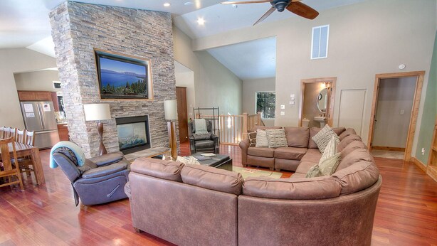 A spacious living room with a stone accent wall, a fireplace, leather sofas, and a dining area with wooden furniture. - Enormous luxury cabin rental in unbeatable South Tahoe location (South Lake Tahoe)